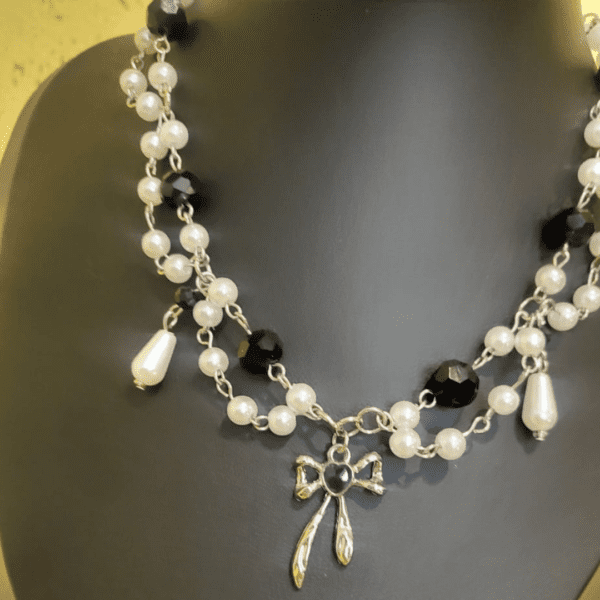 Handmade black and pearl beaded necklace featuring a silver bow charm, crafted by Nel's Jewels.