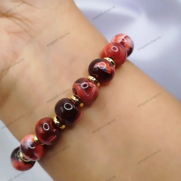 Handmade red ceramic bead bracelet with gold-plated spacer beads, worn on a wrist.