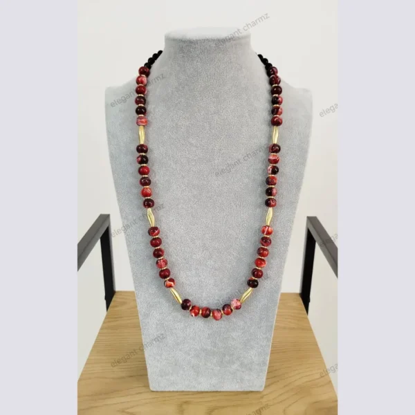 Handmade ceramic bead necklace in red and black tones with gold accents, displayed on a gray bust stand.