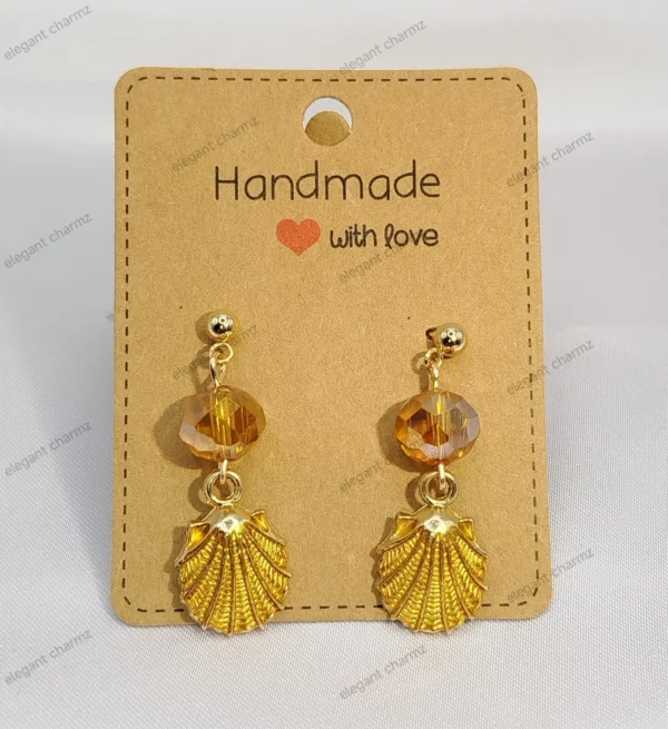 A pair of elegant golden glow crystal dangle earrings with faceted golden crystals, gold-plated shell charms, and stainless steel ear studs, displayed on a handmade jewelry card.