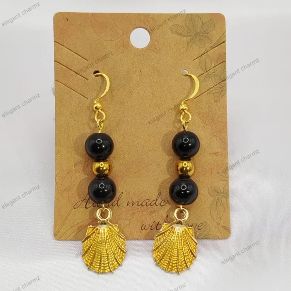 A pair of elegant midnight black bead dangle earrings featuring gold-plated shell charms and stainless steel ear hooks, displayed on a handmade jewelry card.