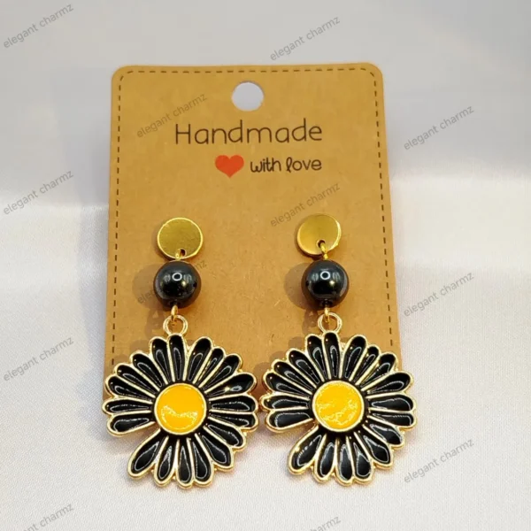 Handmade black daisy flower earrings with gold-tone accents and hematite beads, displayed on a craft paper card.