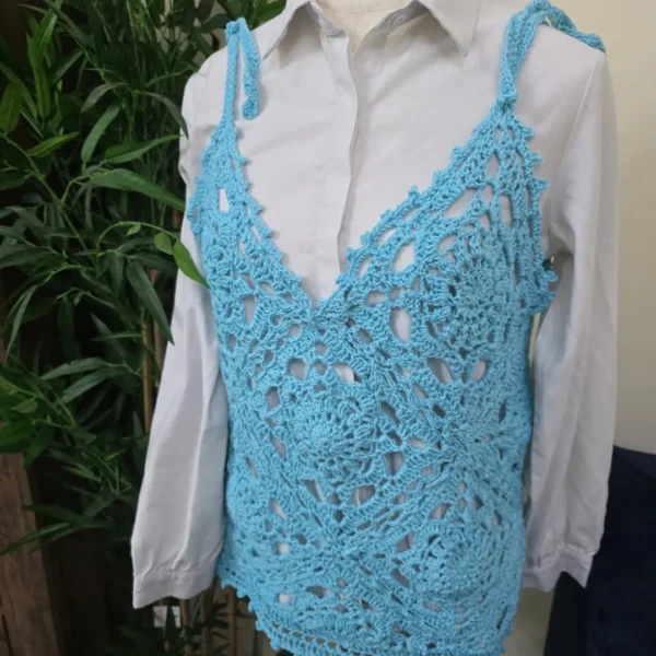 Handmade crochet top in vibrant blue, featuring an intricate lace pattern, worn over a white shirt on a mannequin.