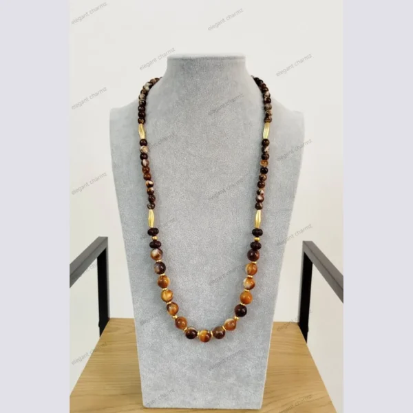 Handmade brown and amber beaded necklace with ceramic and gold-tone accents, displayed on a gray bust stand.