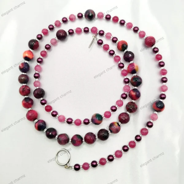 Handmade pink and purple beaded necklace with faceted and pearl-like beads, elegantly laid on a white fabric background.