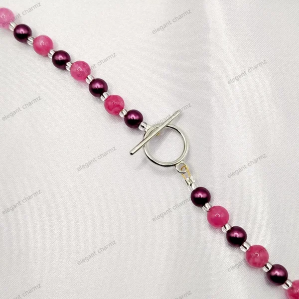 Close-up of a handmade agate-look beaded necklace with a silver toggle clasp, displayed on a white fabric background.