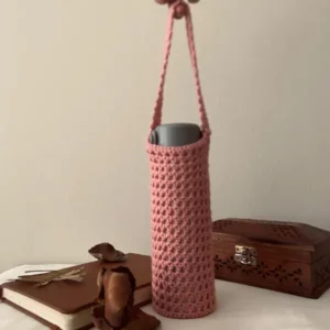 Pink handmade crochet bottle holder hanging vertically with bottle inside